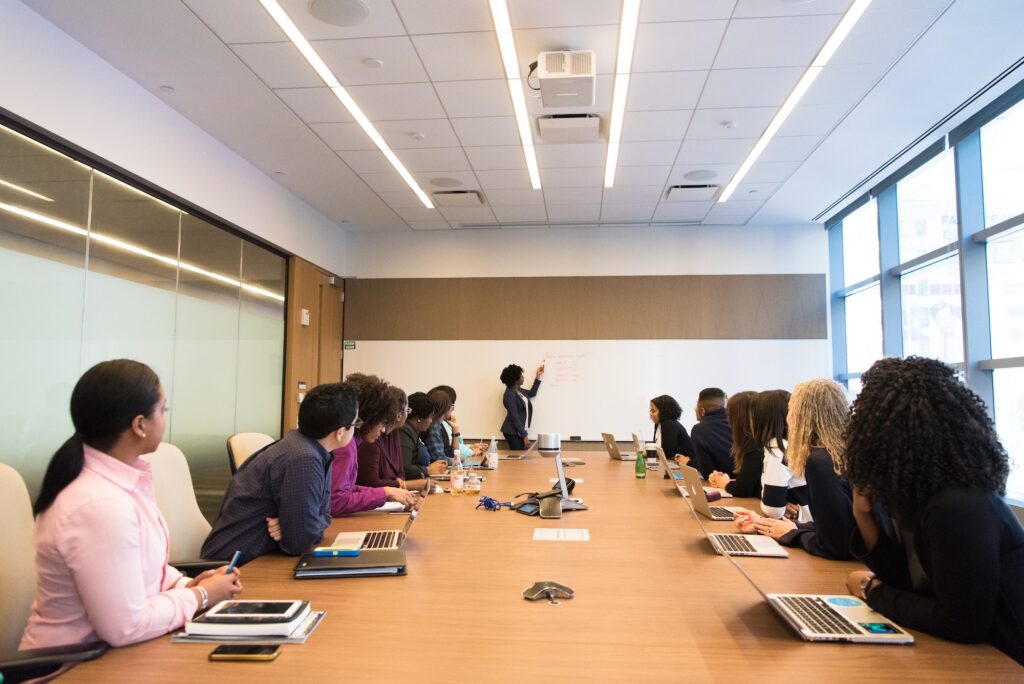 employees sitting around conference table watching a person present on white board